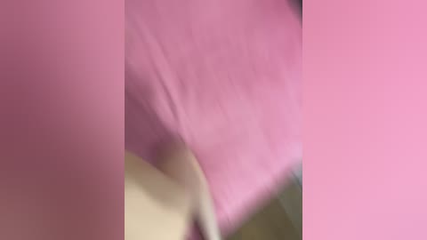 Media: Video of a blurred, close-up shot of a person's arm and hand, wearing a pink shirt. The background is indistinct, with a slight greenish hue, creating a soft, dreamy effect.