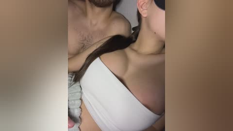 Media: A video captures a close-up of a woman with light skin, large breasts, wearing a white off-the-shoulder top, and a man with a hairy chest.