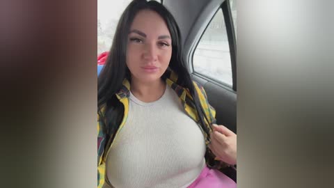 A video of a Latina woman with long black hair, medium skin tone, and a slim figure, wearing a yellow plaid shirt over a white ribbed tank top, sitting in a car.
