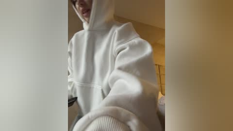Media: A video shows a person wearing a white hoodie, smiling, with blurred indoor background featuring a beige wall and window blinds.