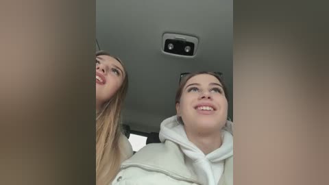 Media: A video of two young women, one blonde with long hair, one brunette with brown hair, smiling inside a car with a beige interior and a sunroof.