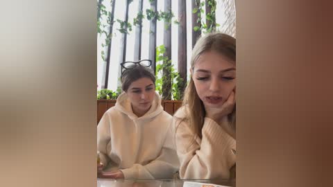 Media: Video of two young women, one with glasses, sitting indoors; the one on the right has blonde hair, wearing a cream sweater.