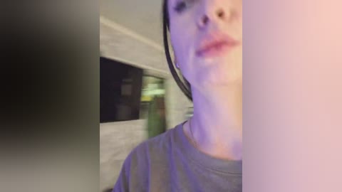 A blurred video of a person with light skin, wearing a gray shirt, standing in a dimly lit room with a TV screen and a green couch in the background.