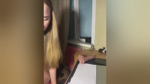 A blurry video of a young woman with long blonde hair, possibly nude, leaning against a mirror in a dimly lit room with beige walls.