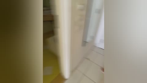 A blurred video of a person, possibly male, wearing a white robe and walking through a dimly lit bathroom with beige walls and tiled floor.