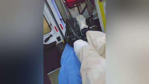 Media: A video showing a person's legs in beige pants and white socks, restrained by black plastic restraints on a blue surface, inside a vehicle. The background includes a red chair and medical equipment.