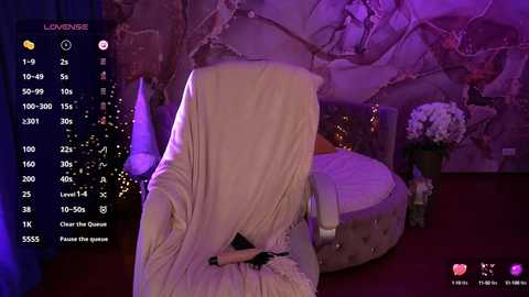 Video of a woman with a white veil covering her face, sitting on a tufted chair in a dimly lit room with a stone wall and purple lighting.