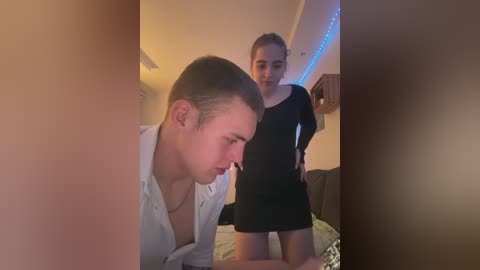 Media: Video of a young man in a light shirt, bending over a woman in a short black dress, in a dimly lit room with blue LED strip lights.