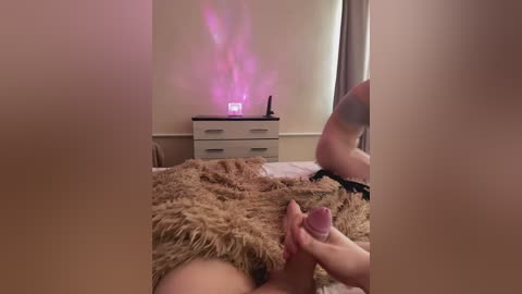 Video of a nude woman lying on a bed, holding her erect penis. Background includes a dresser with a glowing purple light, and a mirror reflects part of the scene.