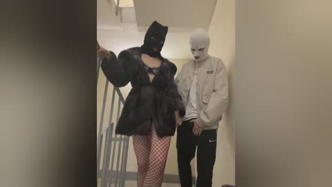 Video of a woman in a black fur coat, fishnet stockings, and a black mask, standing next to a bald man in a beige jacket, in a dimly lit hallway.