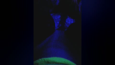 A video of a dark, blurry figure with glowing blue outlines, possibly a person, in a dimly lit room. The figure's facial features are indistinct, creating an eerie, otherworldly atmosphere.