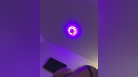 Media: Video of a ceiling-mounted circular LED light emitting a bright purple glow, with a white ceiling and a dark wall in the background.