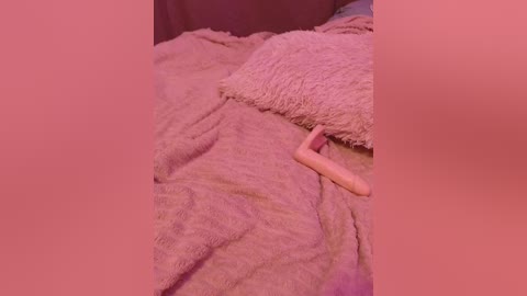 Video of a person sleeping under a soft, fuzzy, light pink blanket, with a plush pillow and a light pink object, possibly a stuffed animal or toy, beside them.