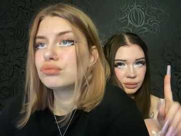 Media: Video of two young women with light skin, one with blonde hair and the other with dark hair. They are dressed in black, with the blonde woman in the foreground making a pouty face and the brunette gesturing with her hand.