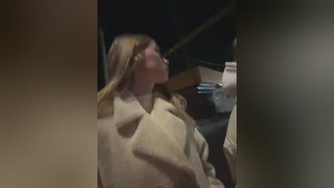 Media: A video of a young blonde woman in a beige robe, with her back to the camera, sitting on a dark wooden bench. The background is dimly lit, suggesting an indoor setting.