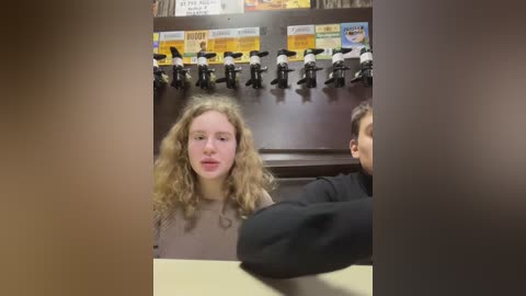 Media: Video of a young woman with curly blonde hair and fair skin, seated at a counter in a fast-food restaurant. She wears a beige shirt and appears calm. Behind her, multiple drink dispensers and menu signs are visible.