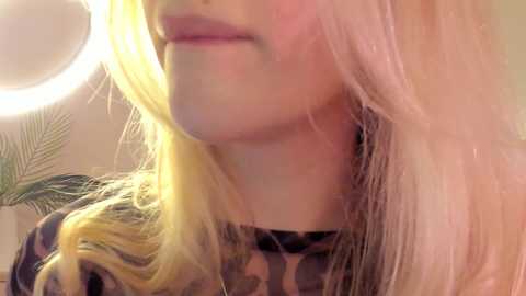 Media: Video of a woman with long, blonde hair, wearing a patterned camo shirt, partially illuminated by a bright, round light.