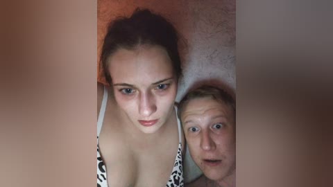 Video of a young woman with light skin and dark hair, wearing a leopard-print bra, standing in front of a man with pale skin and short hair. The background is blurred.