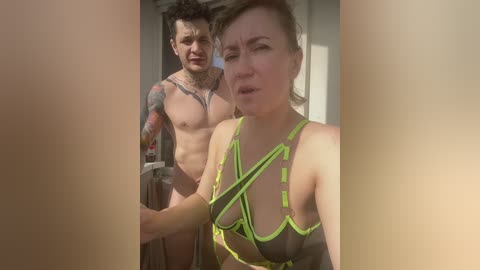 A video shows a tattooed, muscular man in a doorway, nude except for a neon harness, and a woman with short brown hair in a bikini top.