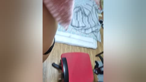 A video of a person's hand with a beige watch on the left, a red chair in the center, and a bed with white sheets and gray pillowcases in the background.