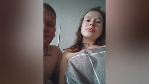 Video of a Caucasian couple, a man with a tattoo on his chest, and a woman with straight brown hair, in a bathroom setting.