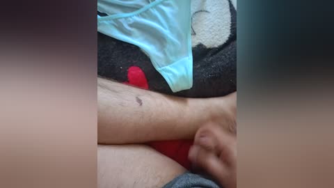 Video of a person's bare legs with a small bruise, wearing light blue panties and a gray blanket with a red bear plush toy, lying on a dark couch.