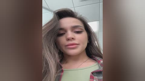 Video of a young woman with long brown hair, fair skin, wearing a green top, captured from a low angle, with blurred background.