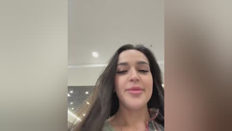 Video of a young woman with long black hair, fair skin, and closed eyes, smiling slightly, taken indoors with a blurred background.