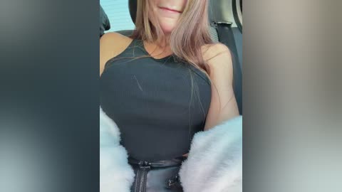 Video of a woman in a black tank top, seated in a car, with her head partially covered by her long brown hair.