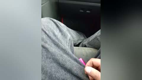 Video of a person's hand inserting a pink key into a car's ignition, wearing gray jeans, inside a dimly lit car with a dark dashboard.