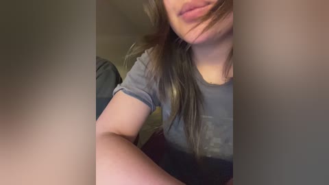Video of a young woman with fair skin, long brown hair, and a gray t-shirt, partially obscured by the camera's lens.