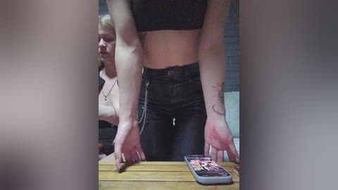 Video of a woman in black leather pants and a black crop top, holding a smartphone with a red, heart-shaped chocolate on it, against a brick wall background.