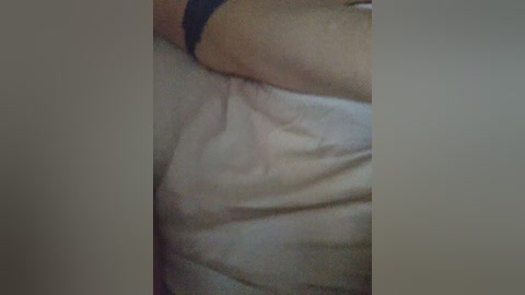 Video of a person's upper body with visible skin folds and a dark wristband on the arm, lying on a white bedsheet. The skin appears light, possibly Caucasian. The image is slightly blurred and dimly lit.
