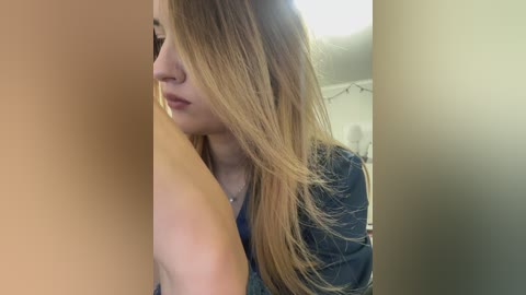 Video of a young woman with long, straight blonde hair, wearing a denim jacket, standing against a beige wall.