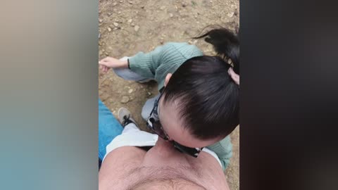 Video of a woman in a green sweater and a girl in a pink dress kissing a man's hairy chest on a dirt path.