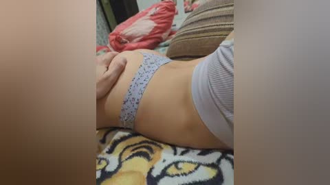 A video captures a light-skinned person wearing light blue polka-dotted panties, lying on a bed with a tiger-print blanket. The background shows a pillow and a stuffed animal.