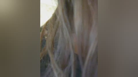 A blurred, soft-focus video shows a person with long, flowing hair and a partially visible face, standing against a dimly lit, indistinct background. The image has a dreamy, ethereal quality.