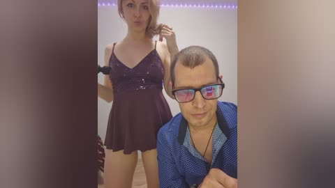 A video of a woman in a dark, sequined dress and a man in a blue shirt with glasses, both in a dimly lit room with purple LED strip lights.