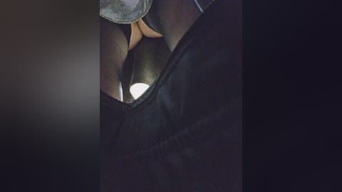 A close-up video of a person's hand holding a small, white, cylindrical object, partially obscured by dark fabric, creating a dramatic, moody atmosphere with shadows.