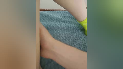 Video of a close-up view of a person's bare thighs on a blue textured blanket. The person is wearing bright yellow socks, and the background is blurred with green and beige tones.