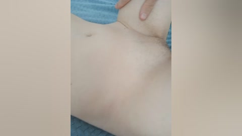 Video of a close-up view of a nude person's upper body, focusing on their lower abdomen and genitals. The person's skin is light and smooth. A hand rests gently on their stomach. Background shows a blue fabric surface.