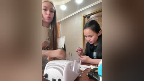 Video of a young girl painting nails in a dimly-lit room. She has long dark hair and wears a black top. The room has beige walls and a wooden door.