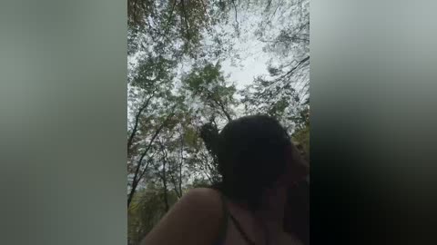 A video captures a woman with short, dark hair, wearing a sleeveless top, standing in a forest with misty trees and a cloudy sky, creating a serene, ethereal atmosphere.