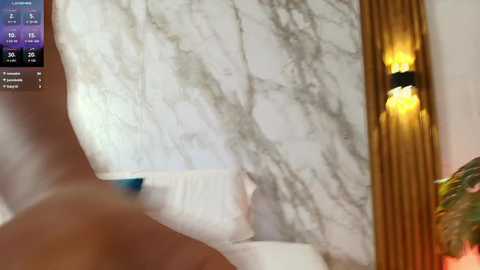 Video of a marble countertop with veined patterns, illuminated by warm, yellow lights. The background includes a blurred, wooden surface and a partially visible person's arm. The image is slightly blurry, suggesting a fast motion or low resolution.