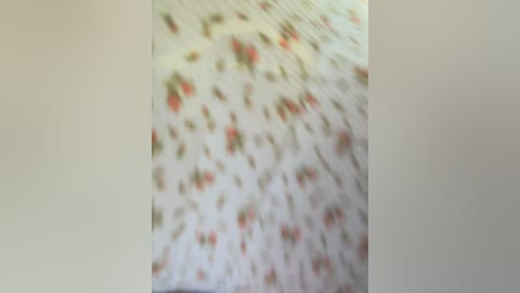 A close-up video of a fabric with a floral pattern in muted colors of red, green, and beige on a white background, slightly blurred, suggesting a textured, possibly woven or embroidered material.