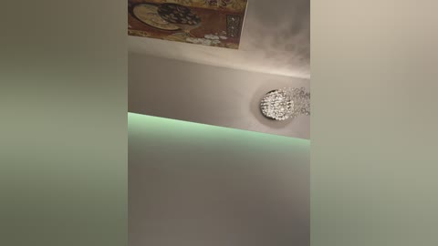 A video of a modern, minimalist ceiling with a circular, crystal chandelier and a section of beige wall partially covered by a textured, off-white ceiling. The image is angled from below, emphasizing the ceiling's soft, smooth surface.
