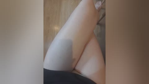 A video showing a close-up of a woman's smooth, pale thigh with a shadow, partially visible black panties, and a wooden floor.