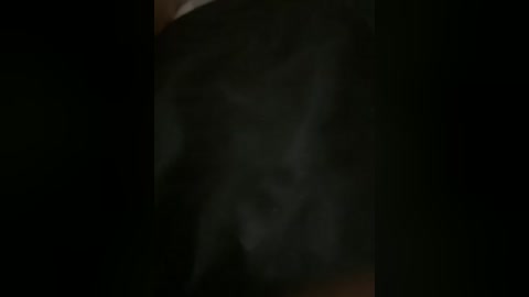 A dimly lit video with a dark, smoky background, featuring an indistinct, shadowy figure standing in the center, partially obscured by the smoke. The image has a moody, mysterious atmosphere.