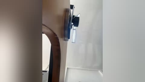 Video of a close-up of a dark, cylindrical ceiling fan with a black cover, mounted on a curved wooden ceiling beam in a modern, minimalist room with white walls.