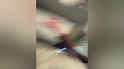 Blurry video of a person with red hair and a pink shirt, possibly female, standing in a dimly lit room with a beige carpet and light-colored walls.